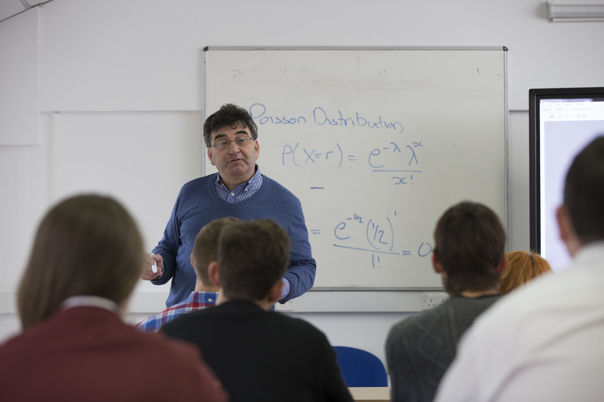 Equations wrote on white board with lecture standing in front teaching to the class