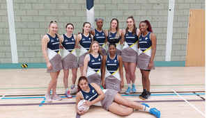 The University of Wolverhampton Womens Netball team, some members standing around others on their knees and one on the floor of the sports hall with a netball