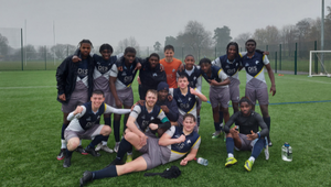 The University of Wolverhampton Mens football team, standing and sitting with arms around each other in the middle of a pitch outdoors, all wearing University of Wolverhampton uniforms