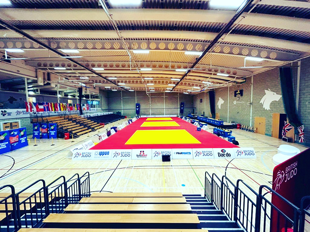 Judo mats prepared in the University sports hall, overseen by rows of seats
