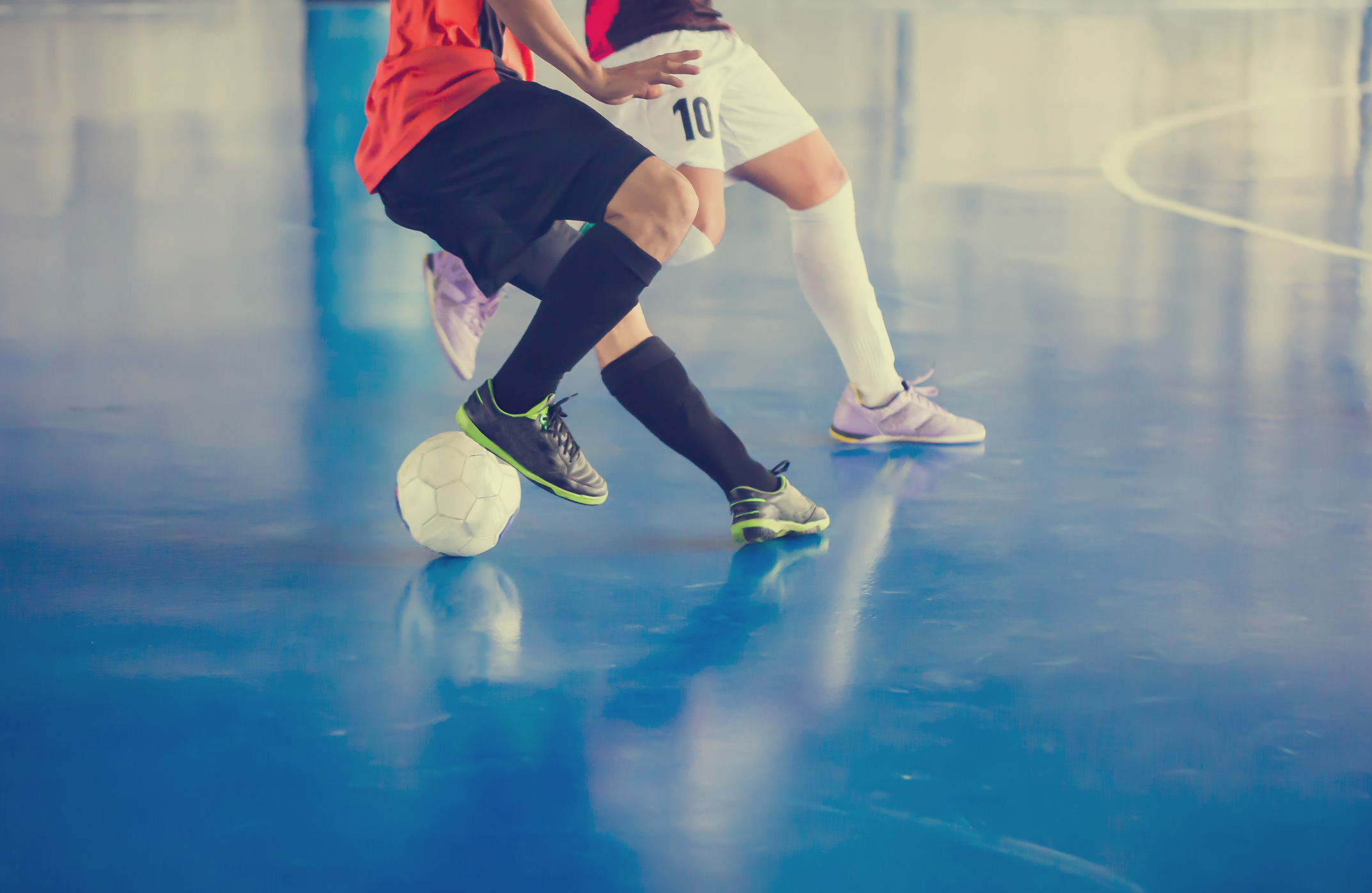 People playing futsal on a blue indoor pitch, wearing uniforms and sports trainers