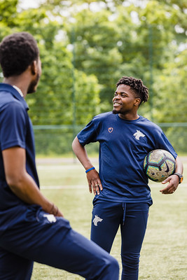 A student at Walsall campus holding a football while another looks at him, both wearing University of Wolverhampton uniforms