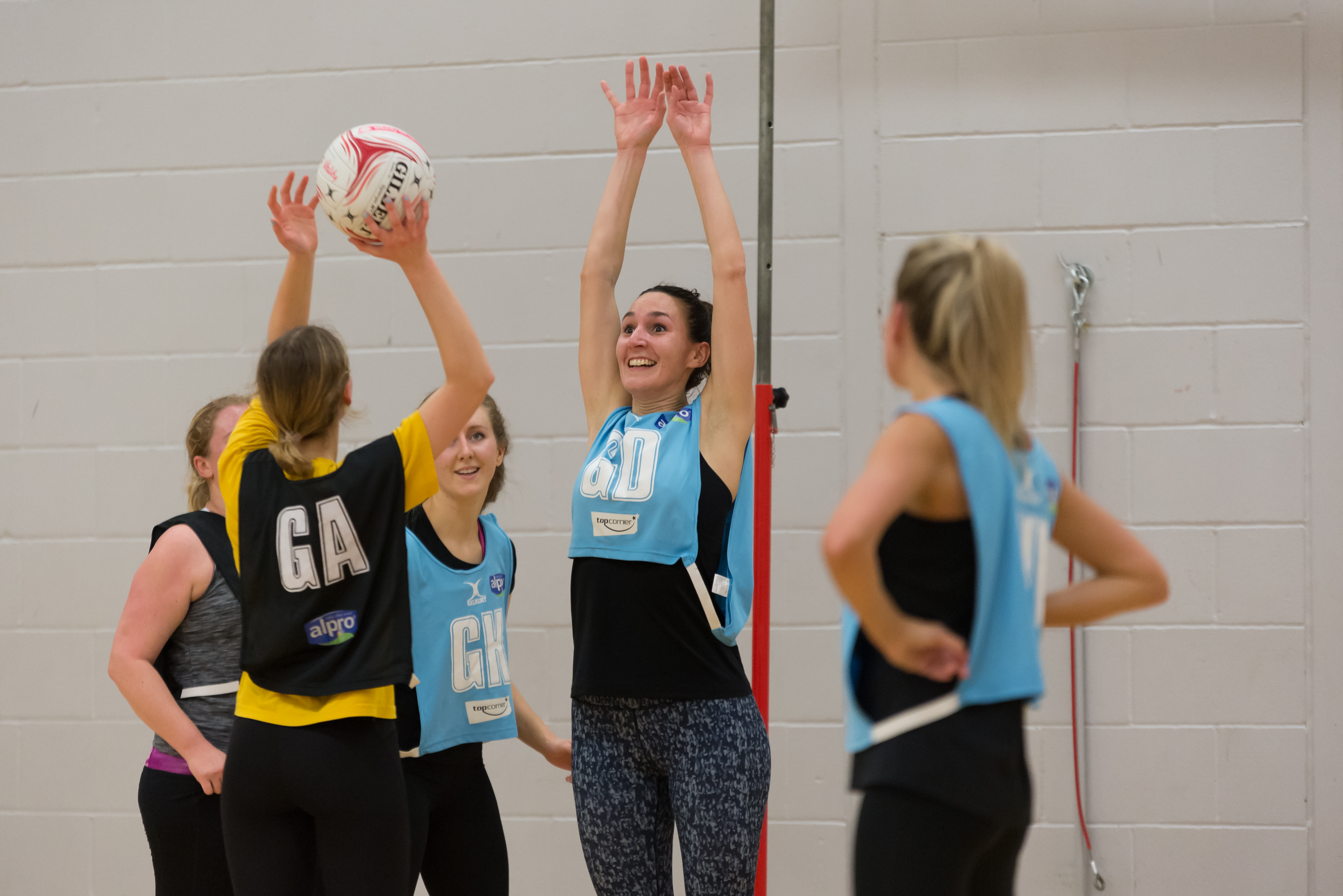 Netball players in opposing team colours, one preparing a shot while another blocks her