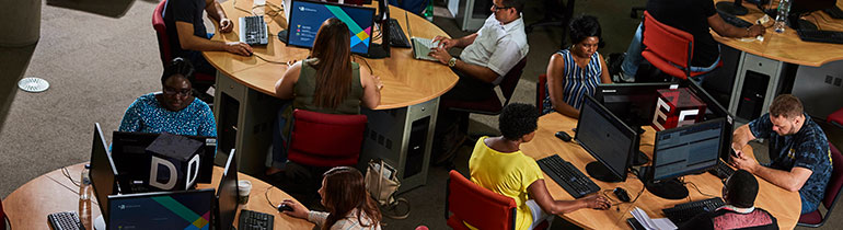 Several computer desks with four students each around them, working on desktop setups